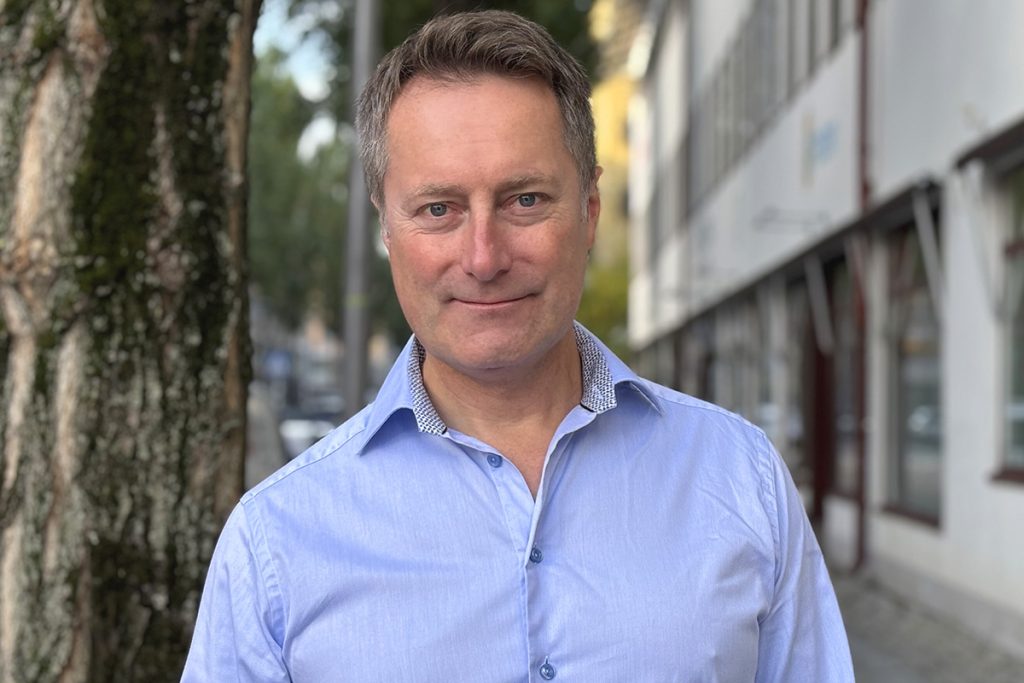 Leende medelålders vit man i blå skjorta som står ute på gatan